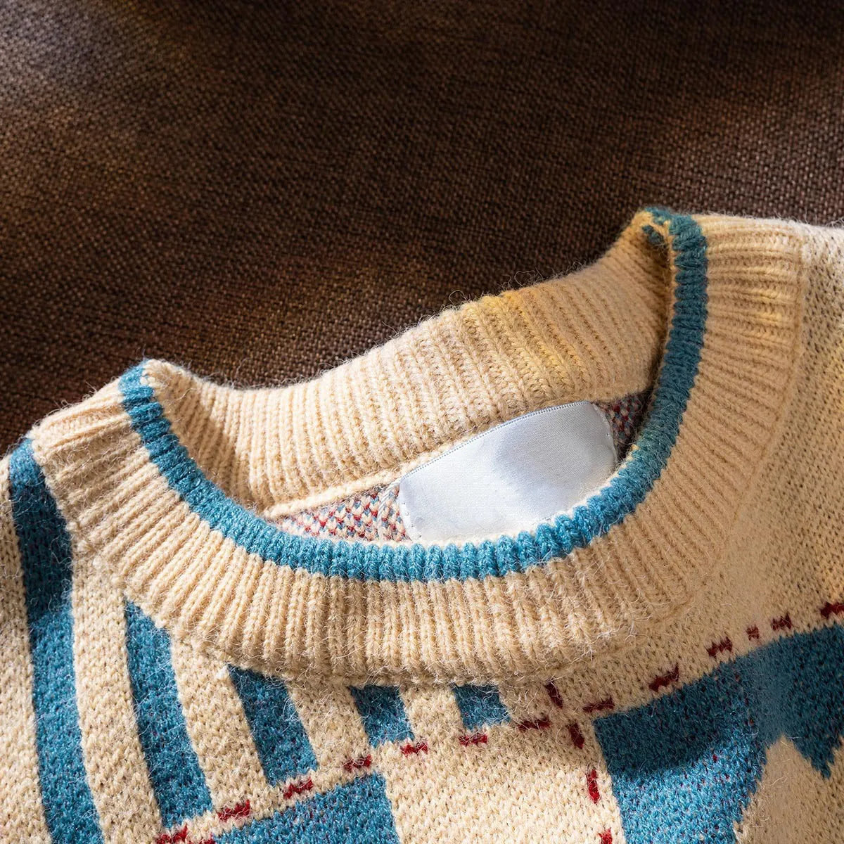 Close-up of a beige sweater with blue and red pattern on a brown background