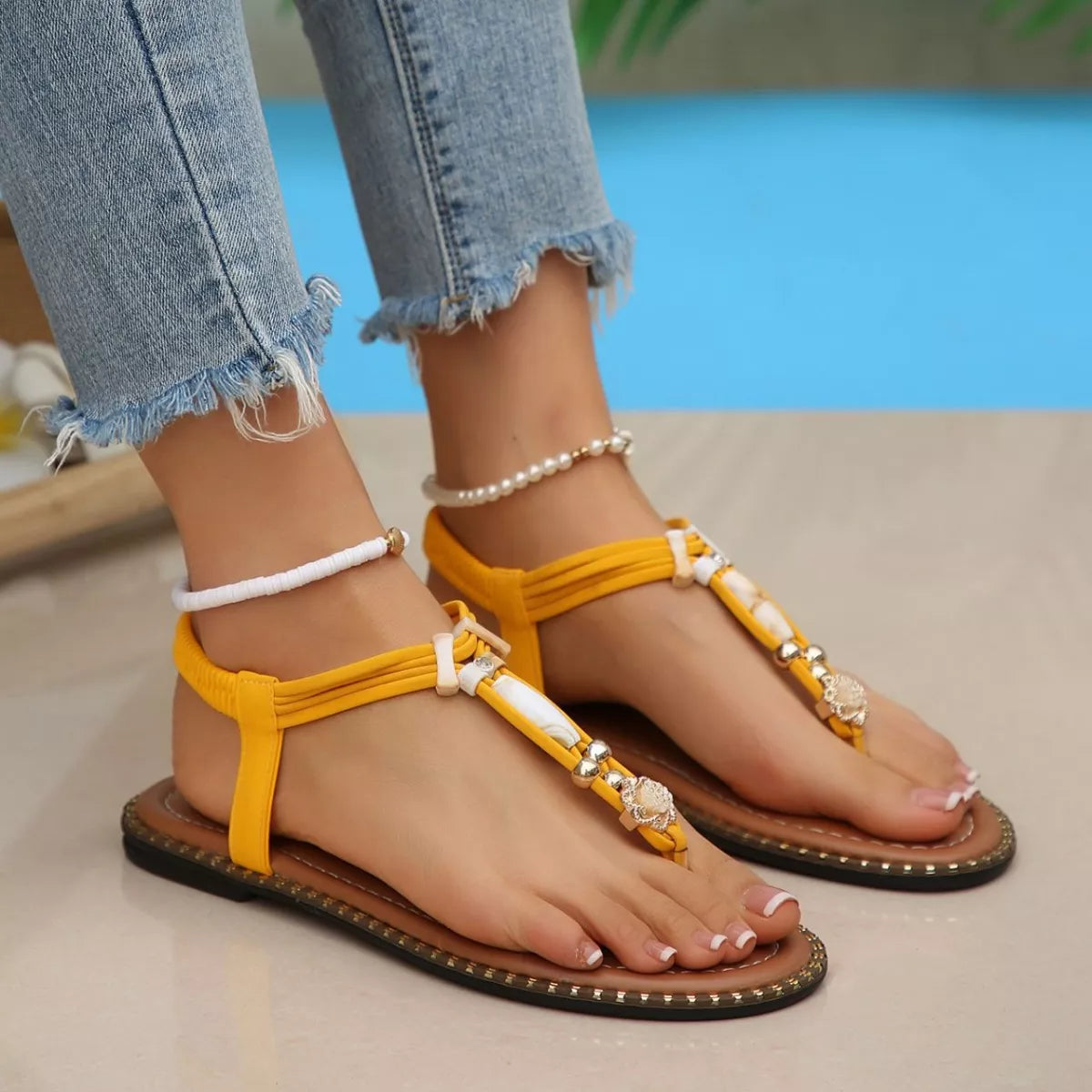 Yellow sandals with decorative straps worn by a person sitting by a pool.