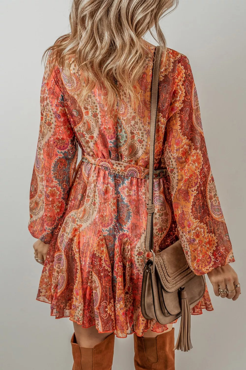 Person wearing a patterned dress with long sleeves and brown boots, holding a brown handbag.