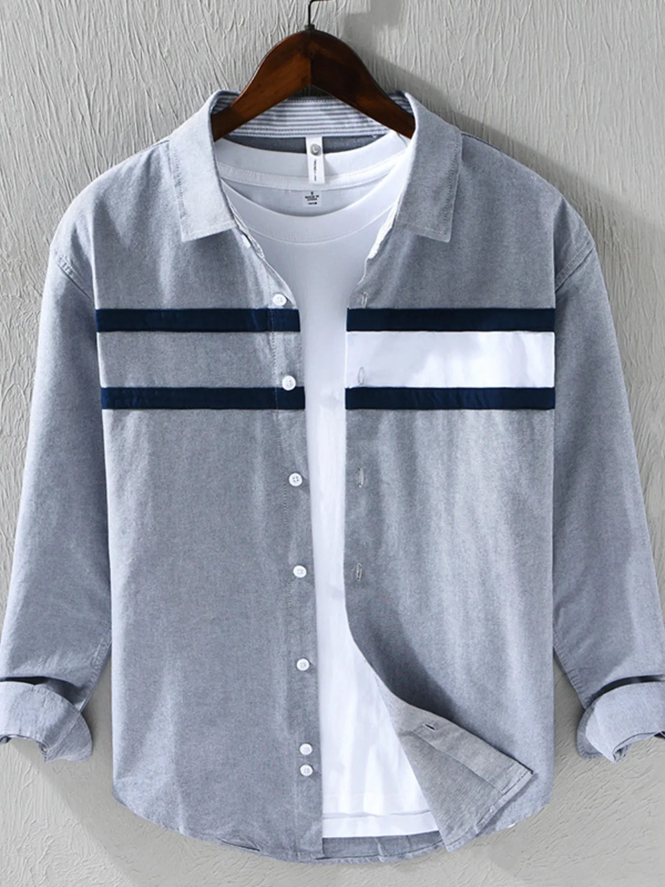 Gray button-up shirt with white collar and navy stripes on a hanger against a gray background