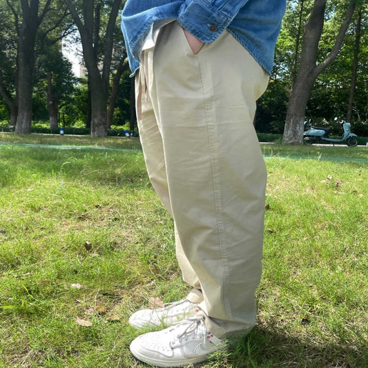 Person wearing beige pants and a blue denim jacket standing on grass with trees in the background