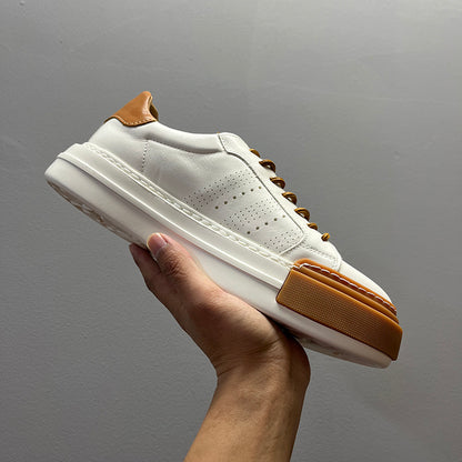 White sneaker with brown accents held against a gray background