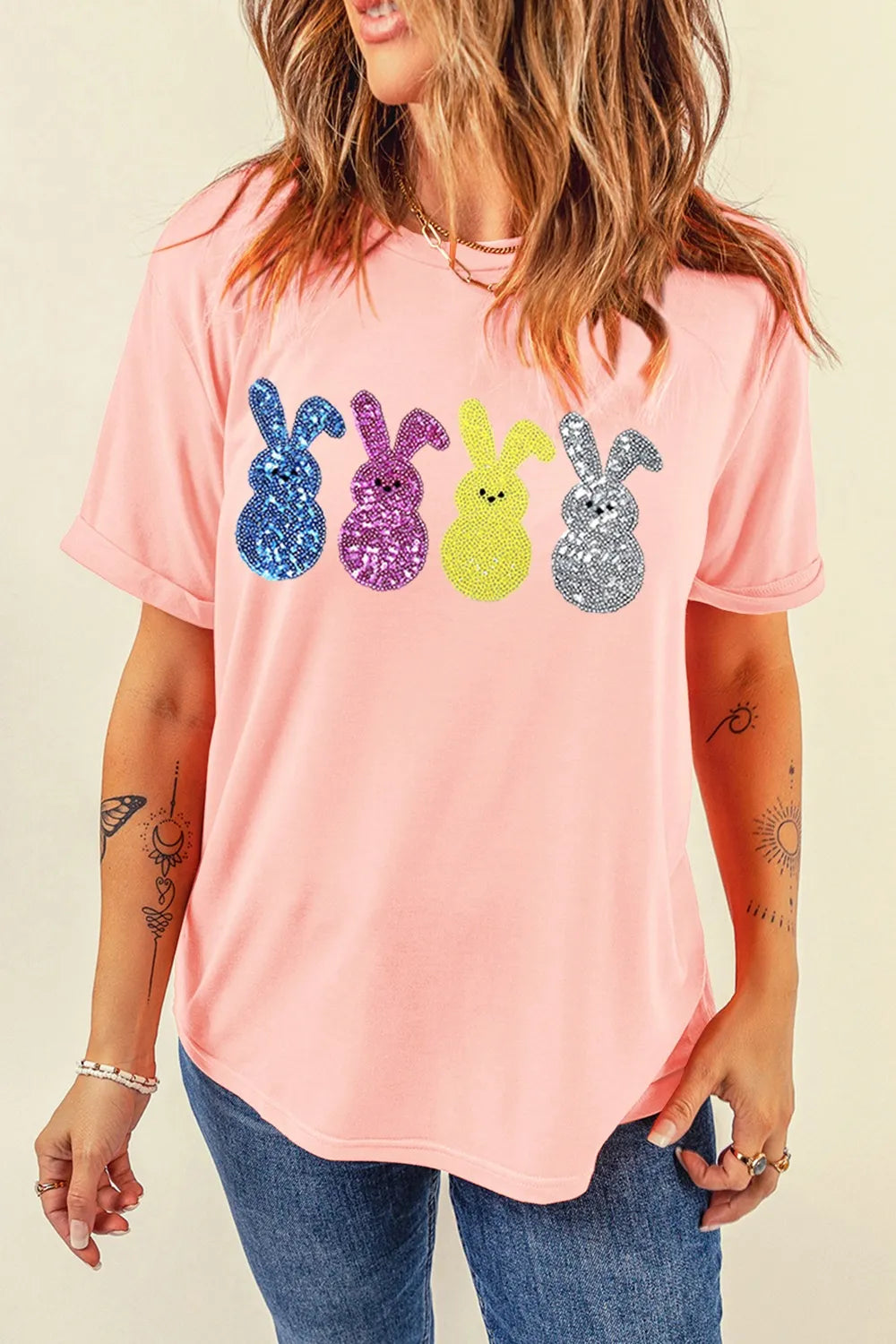 Person wearing a pink t-shirt with colorful glittery bunny designs on a beige background