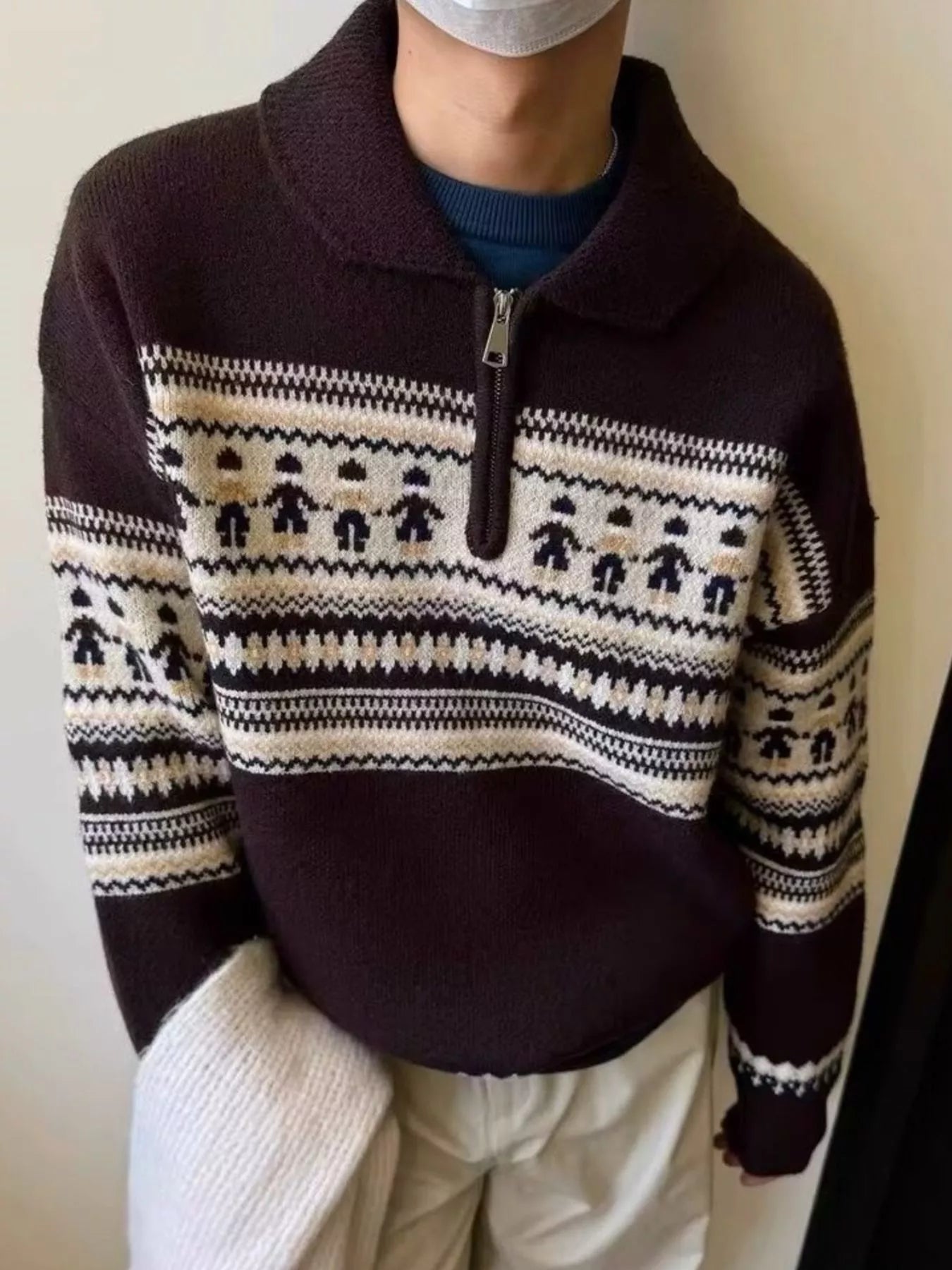 Person wearing a dark brown sweater with a white pattern, standing against a plain background.