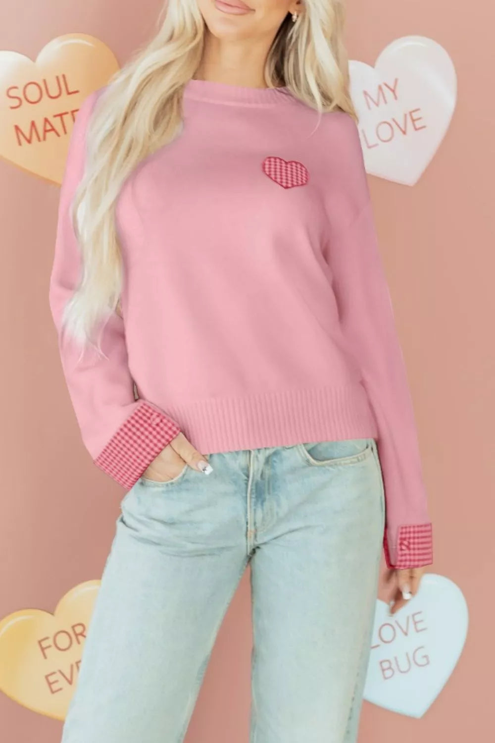 Person wearing a pink sweater with a heart design against a pink background with heart-shaped text.