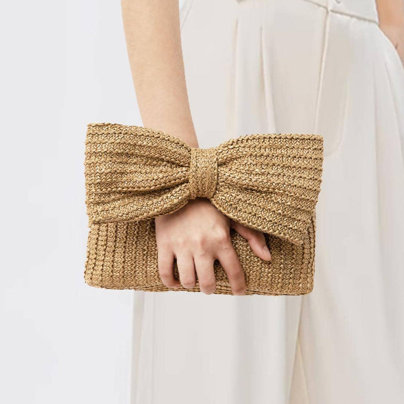 Person holding a woven clutch with a large bow design against a plain background