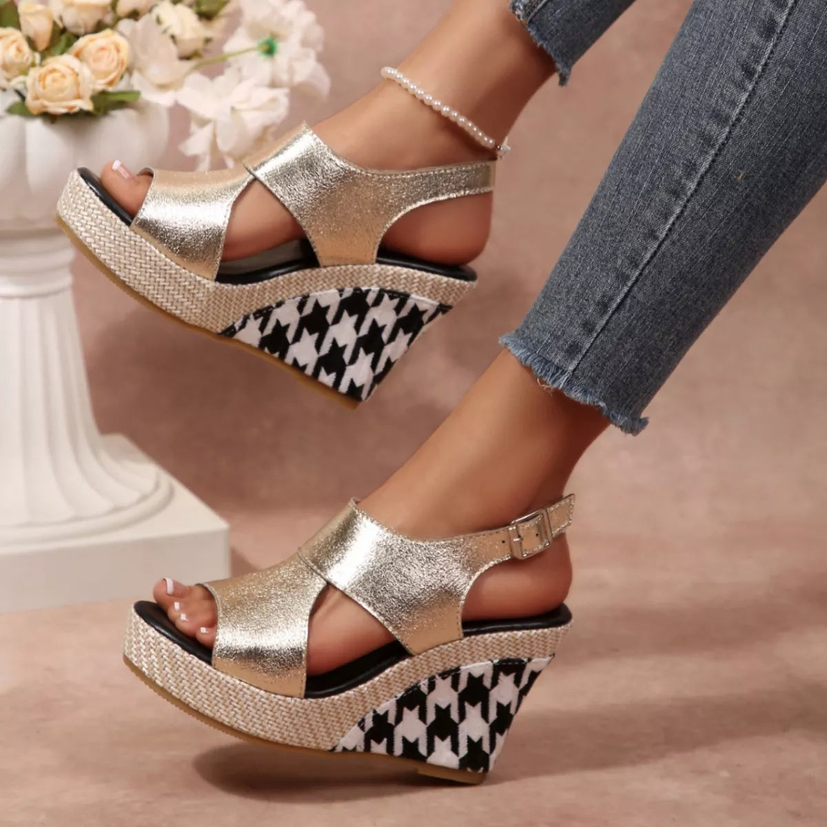 Gold wedge sandals with houndstooth pattern worn by a person, with a blurred floral 
