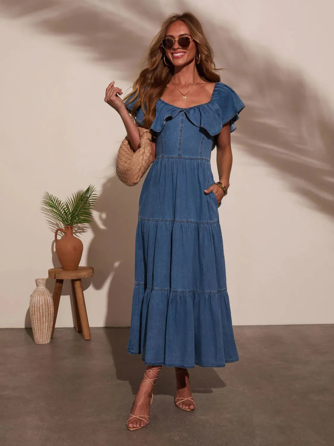 Woman in a blue dress standing indoors with a plant and vase in the background