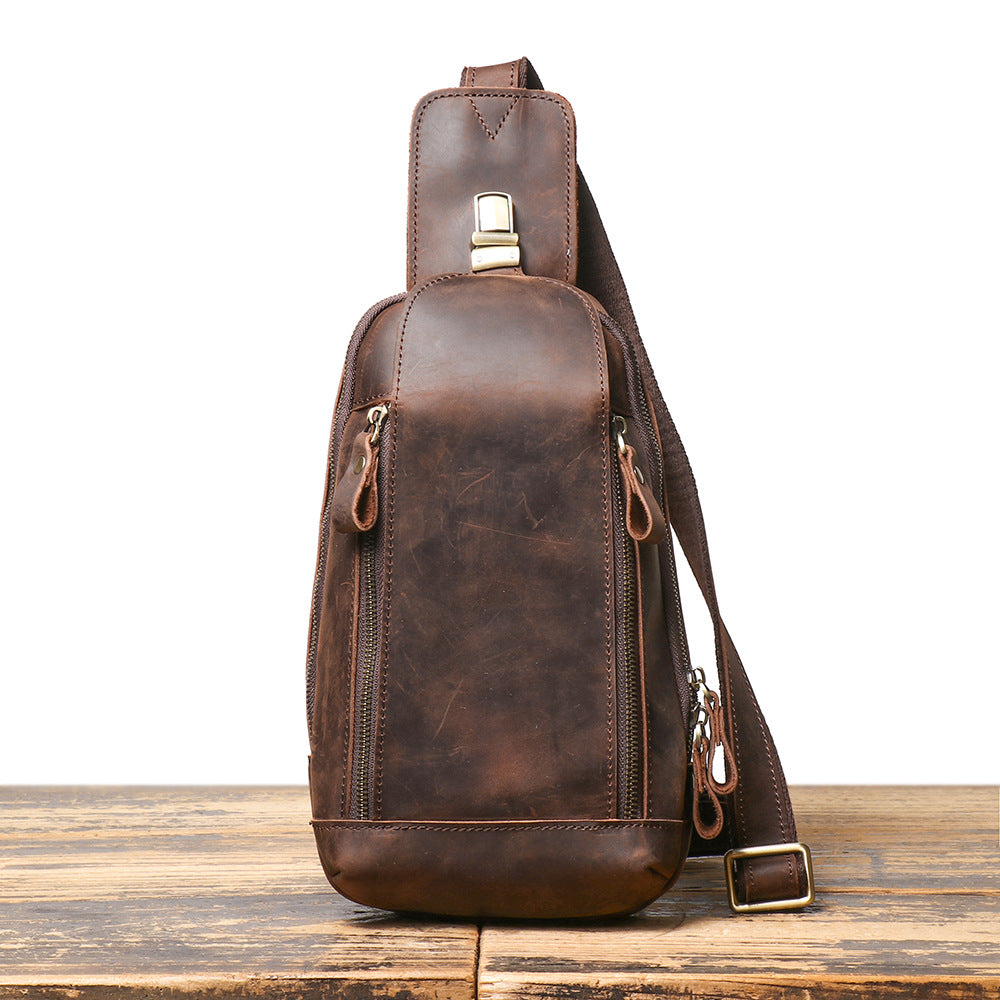 Brown leather sling bag on a wooden surface with a white background