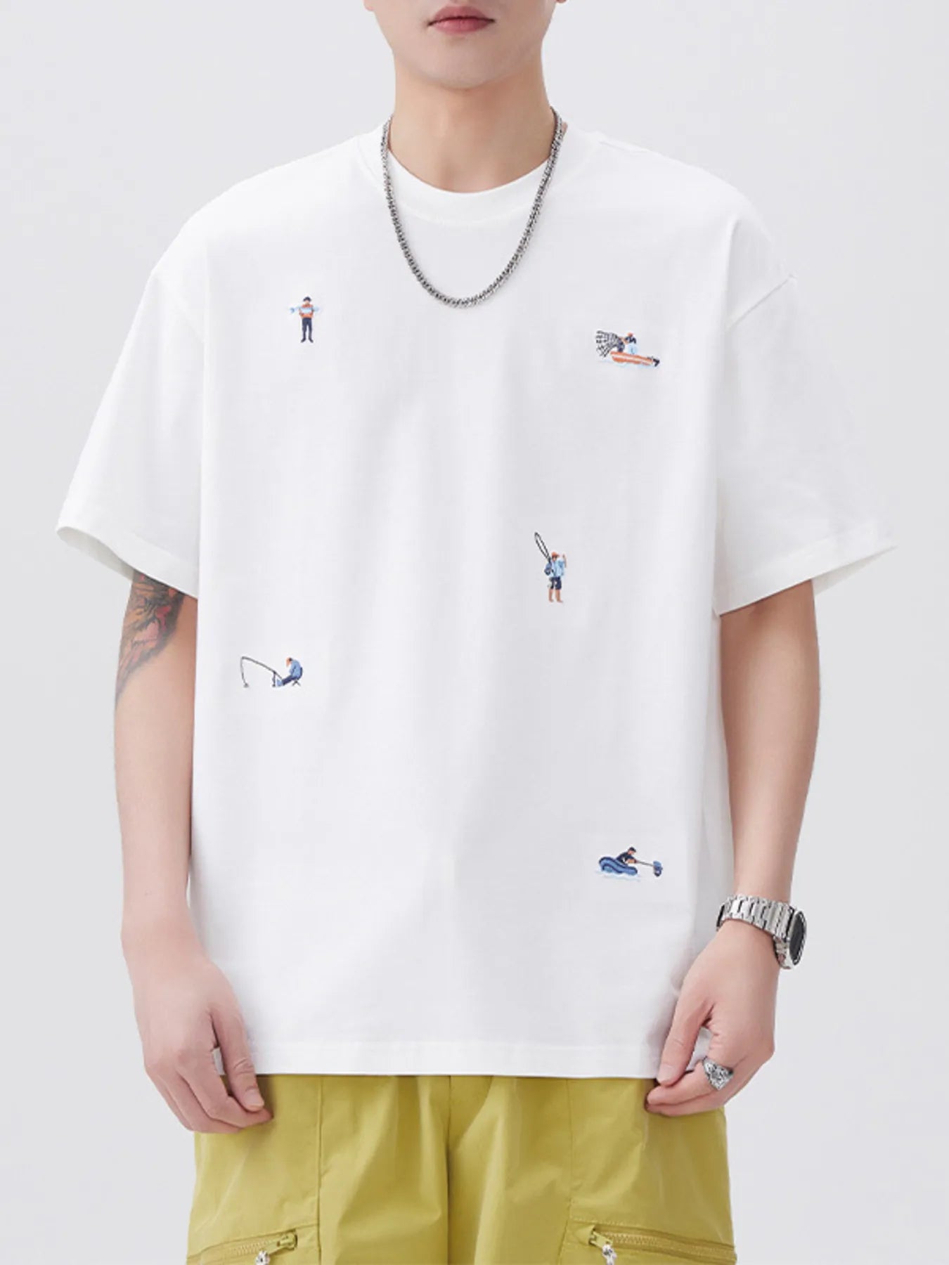 Person wearing a white t-shirt with small embroidered designs on a plain background
