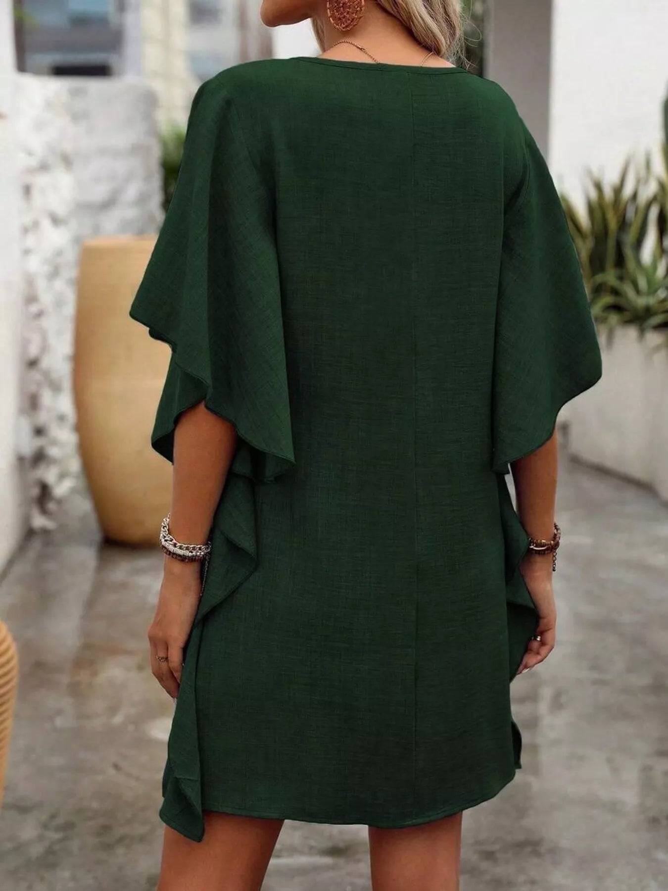 Person wearing a green dress with ruffled sleeves in an outdoor setting.