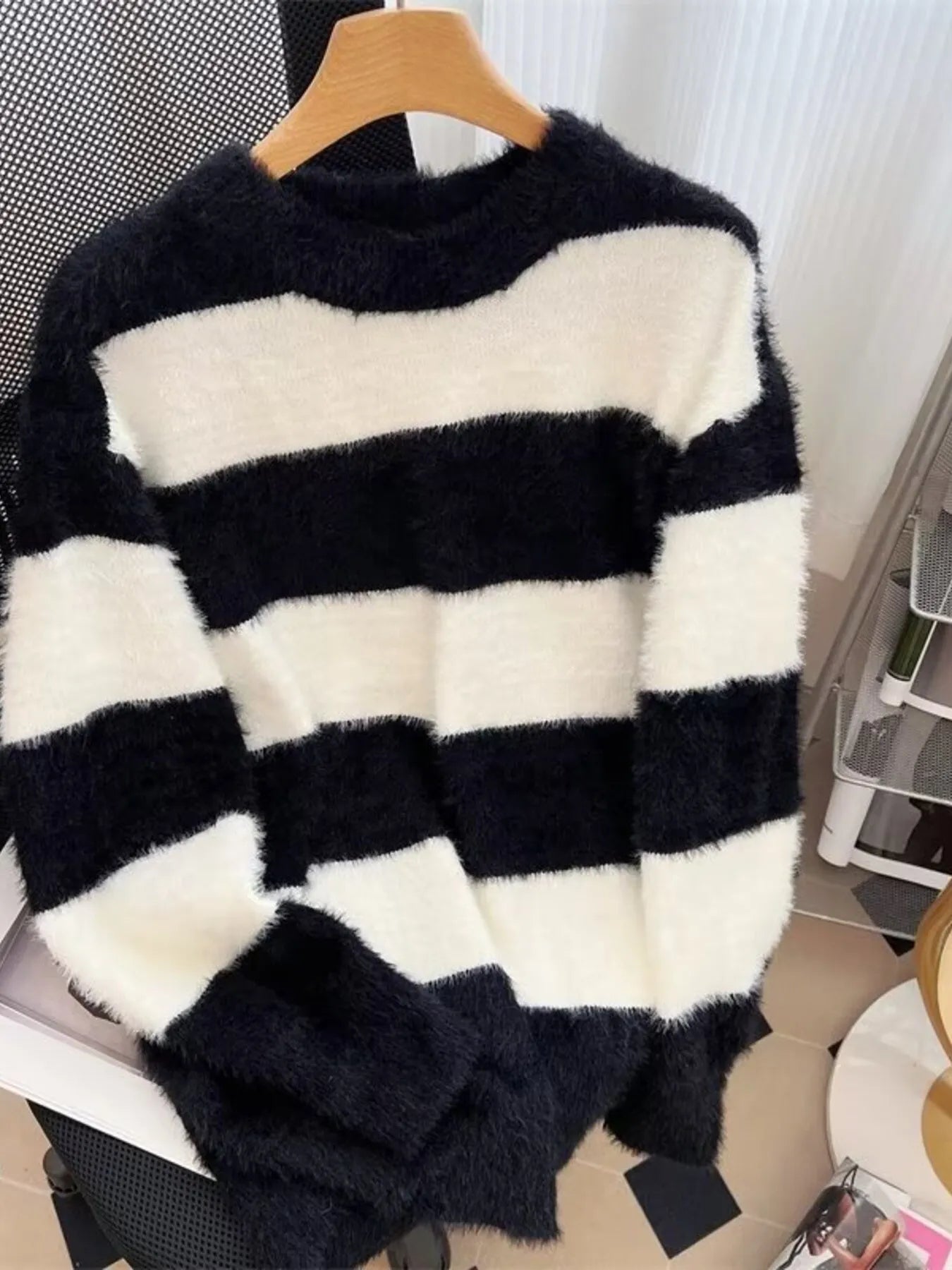 Black and white striped sweater on a hanger against a neutral background
