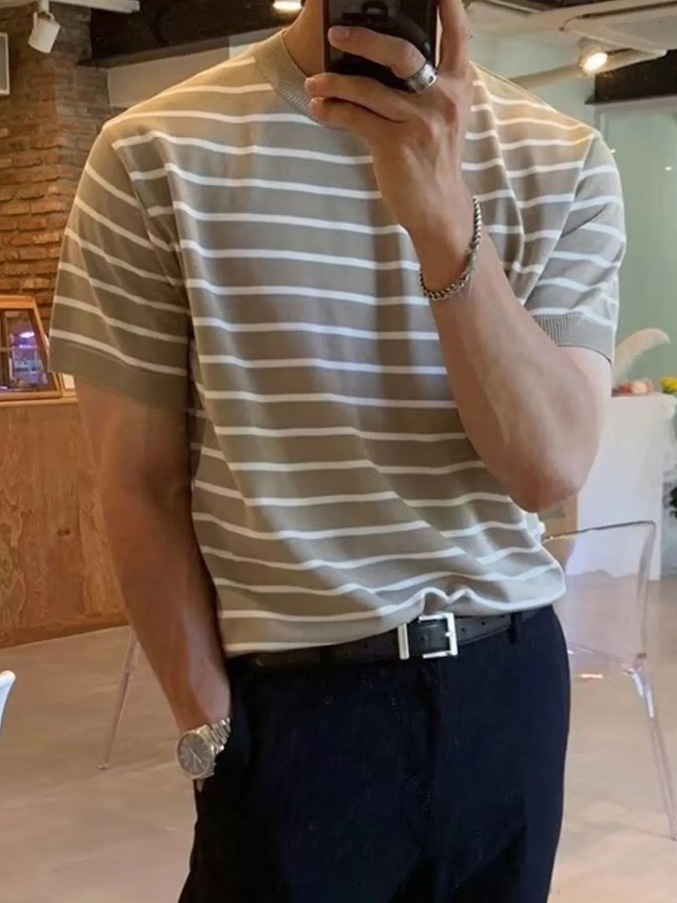 Person wearing a striped shirt taking a mirror selfie indoors.