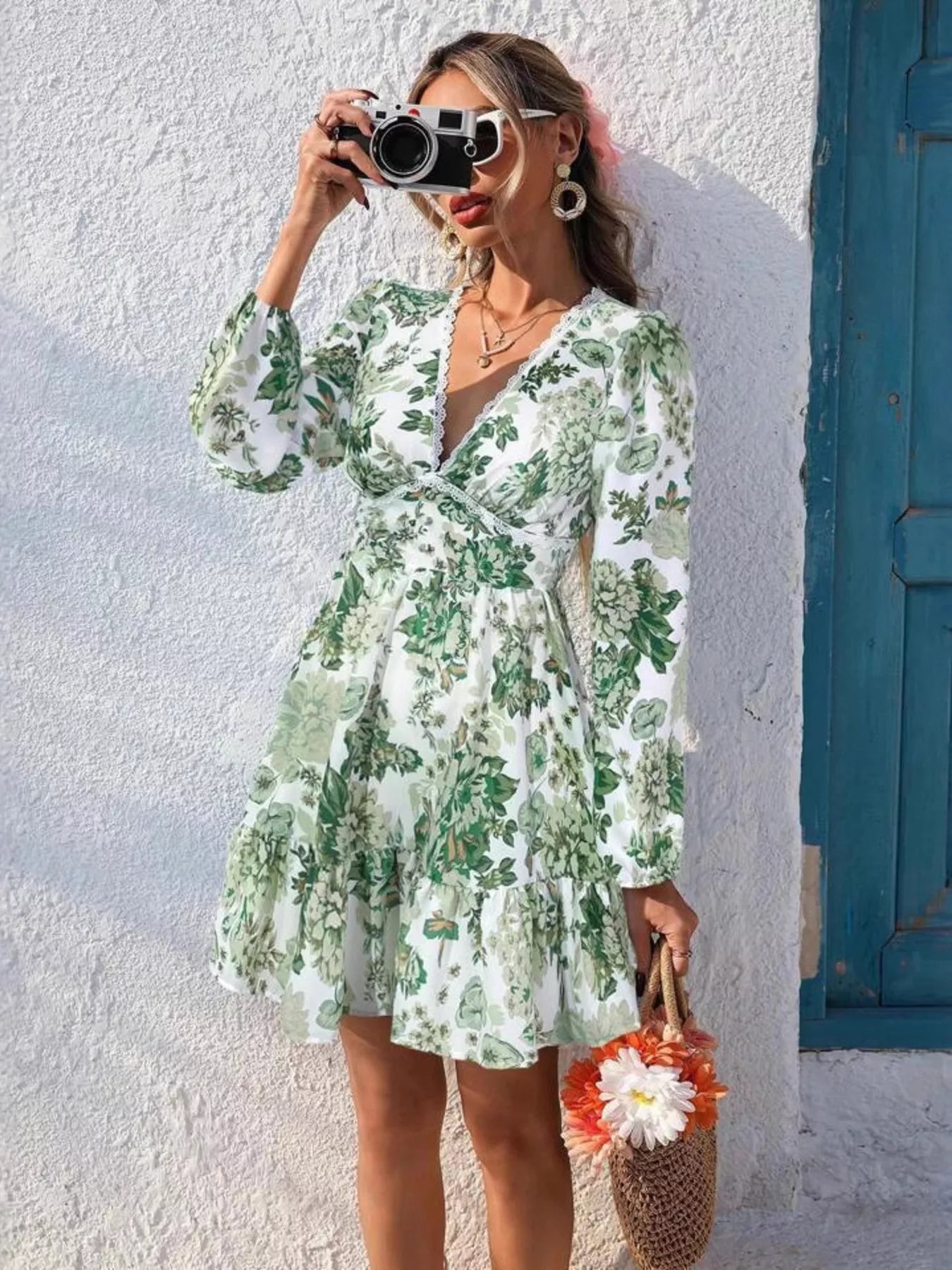 Woman in a green floral dress taking a selfie against a white wall with a blue door.