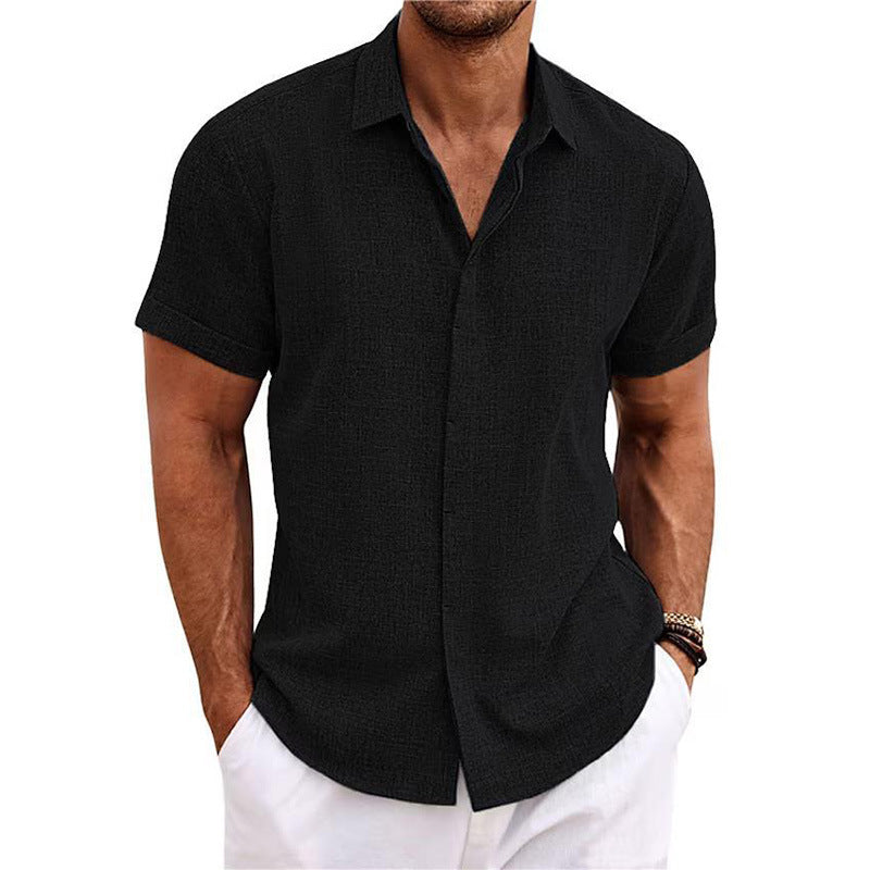 Man wearing a black short-sleeve button-up shirt and white pants on a white background
