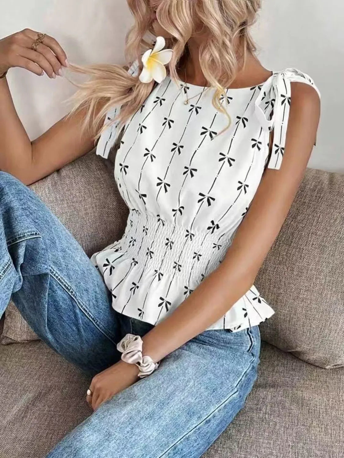 Woman wearing a white blouse with black patterns and blue jeans sitting on a couch.