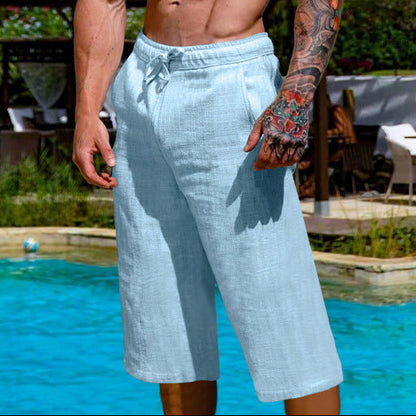 Man with tattoos standing by a poolside wearing light blue shorts.