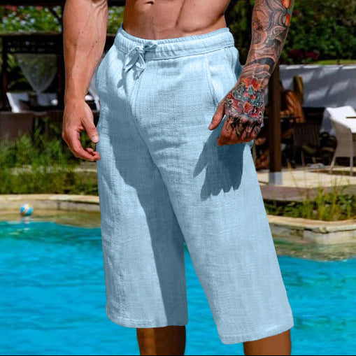Man with tattoos standing by a poolside wearing light blue shorts.