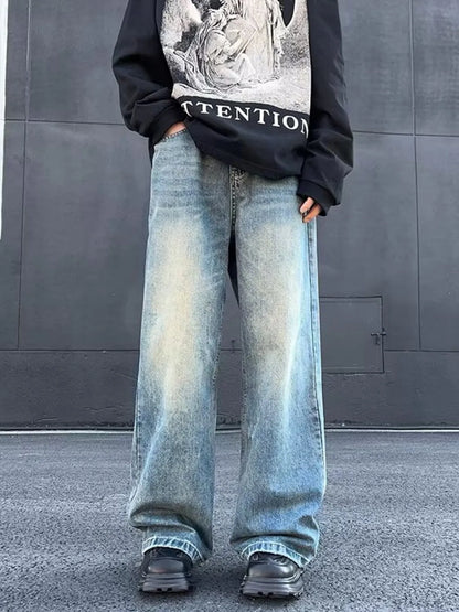 Person wearing a black sweatshirt with graphic design and light blue jeans against a gray wall.
