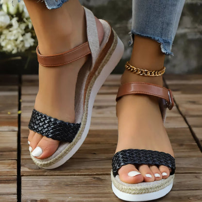 Brown and black wedge sandals on a wooden floor with blurred flowers in the background