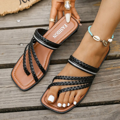 Brown sandals with black braided straps on a wooden surface