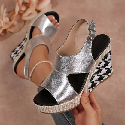 Silver wedge sandals with houndstooth pattern worn by a person, with a blurred floral 