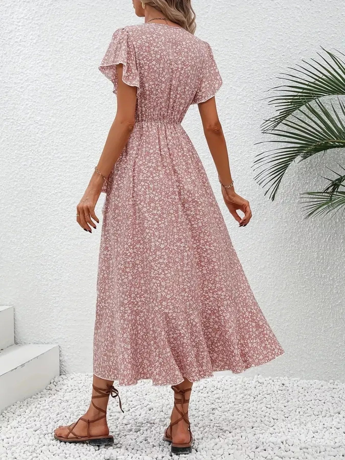 Woman wearing a pink floral dress against a white wall with a plant in the corner.