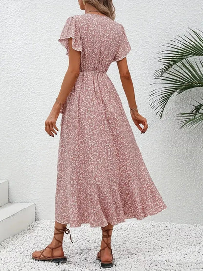 Woman wearing a pink floral dress against a white wall with a plant in the corner.
