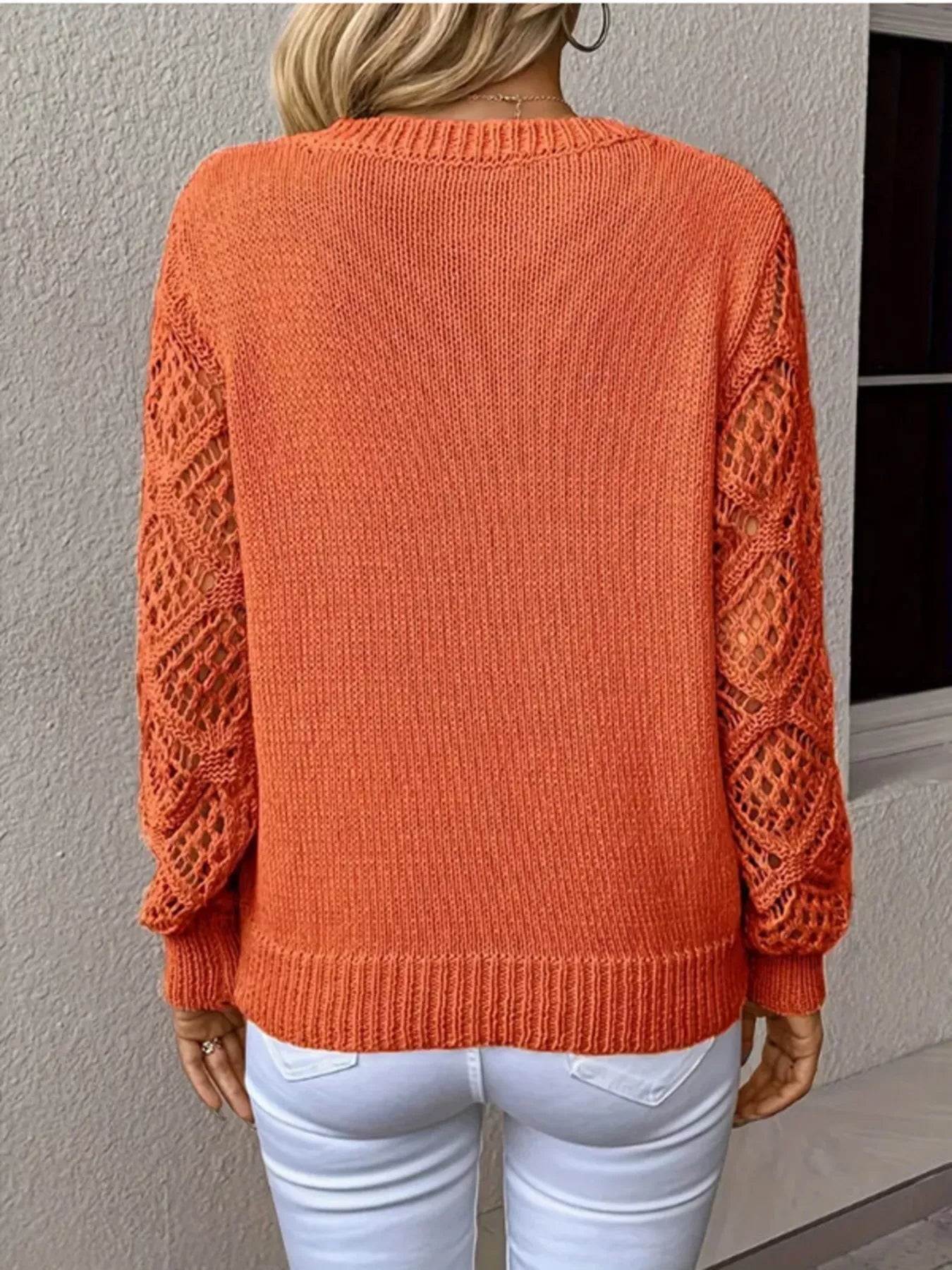 Person wearing an orange sweater with a textured pattern on a plain background
