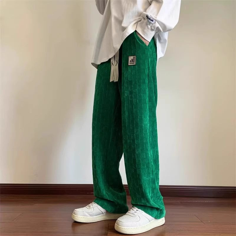 Person wearing green pants and a white shirt against a plain wall.
