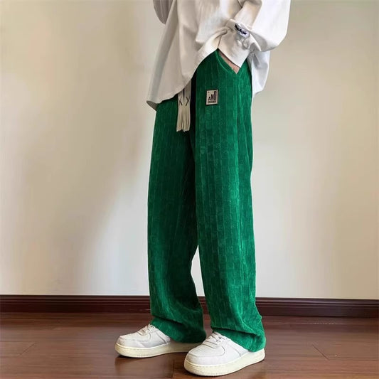 Person wearing green pants and a white shirt against a plain wall.