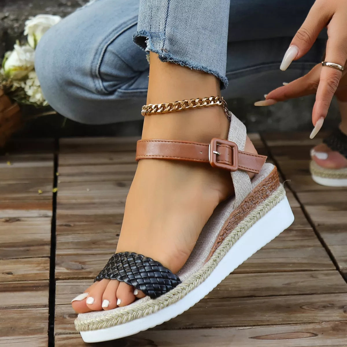 Brown and black wedge sandals on a wooden floor with blurred flowers in the background