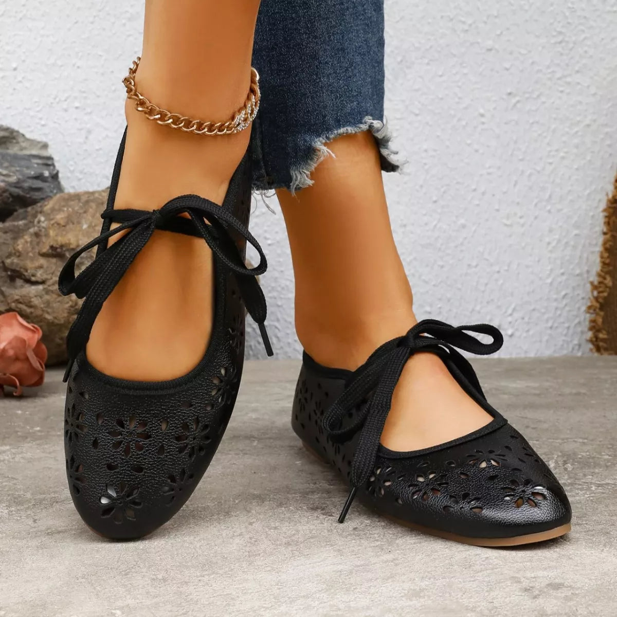 Black perforated flats worn with blue jeans on a neutral background
