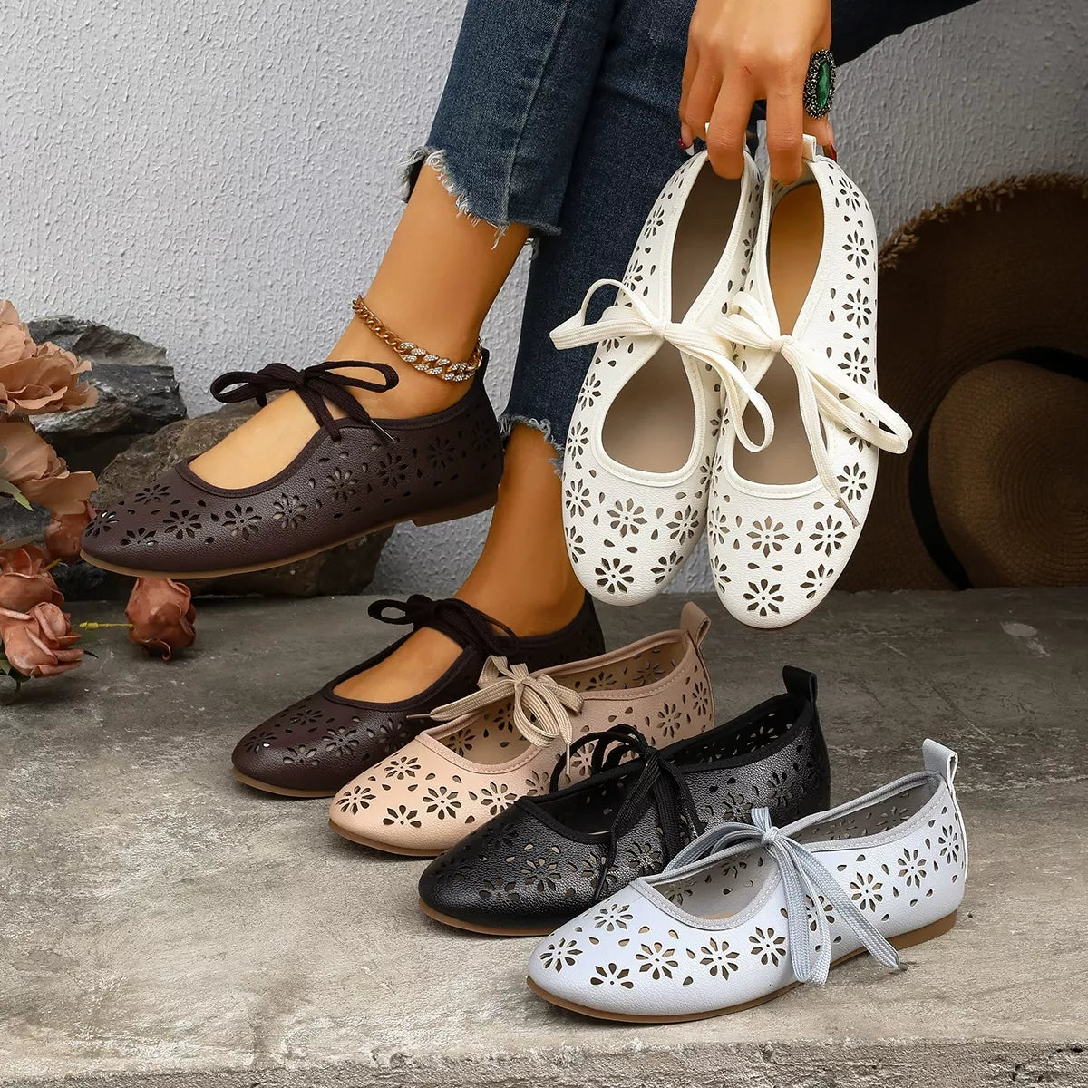 Person holding a pair of white floral-patterned shoes with other colored shoes on the ground.