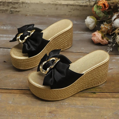 Gold wedge sandals with black bows on a wooden surface