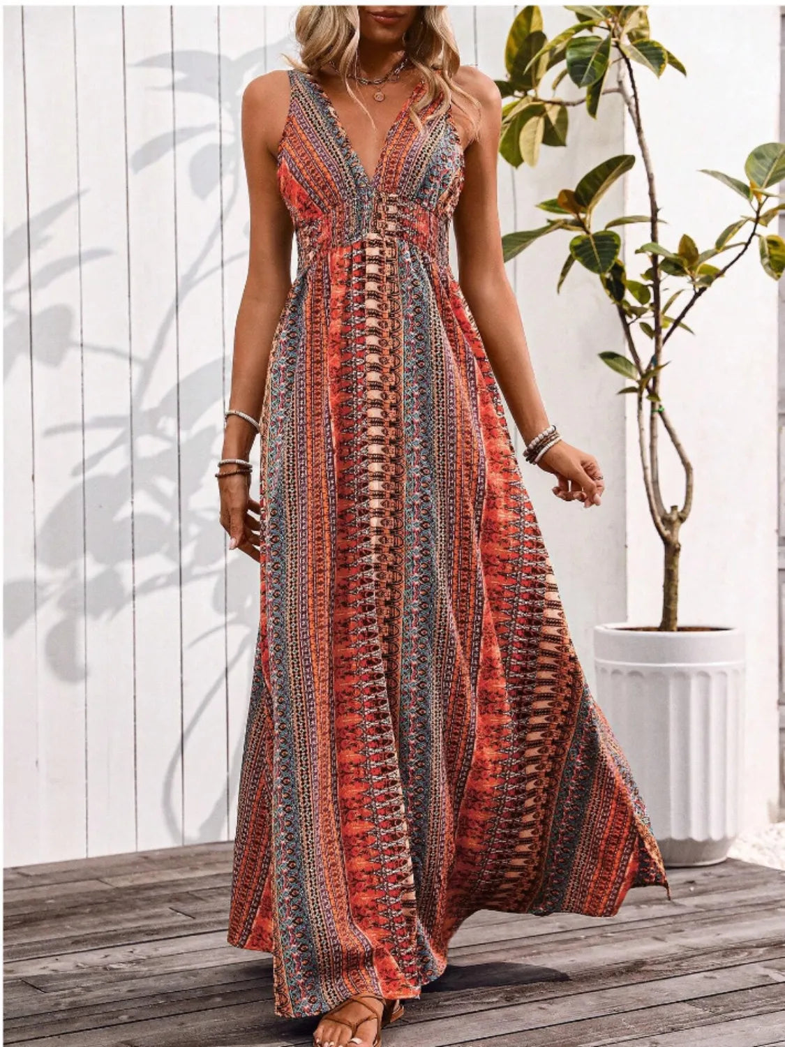 Woman wearing a patterned dress standing on a wooden deck with a plant in the background