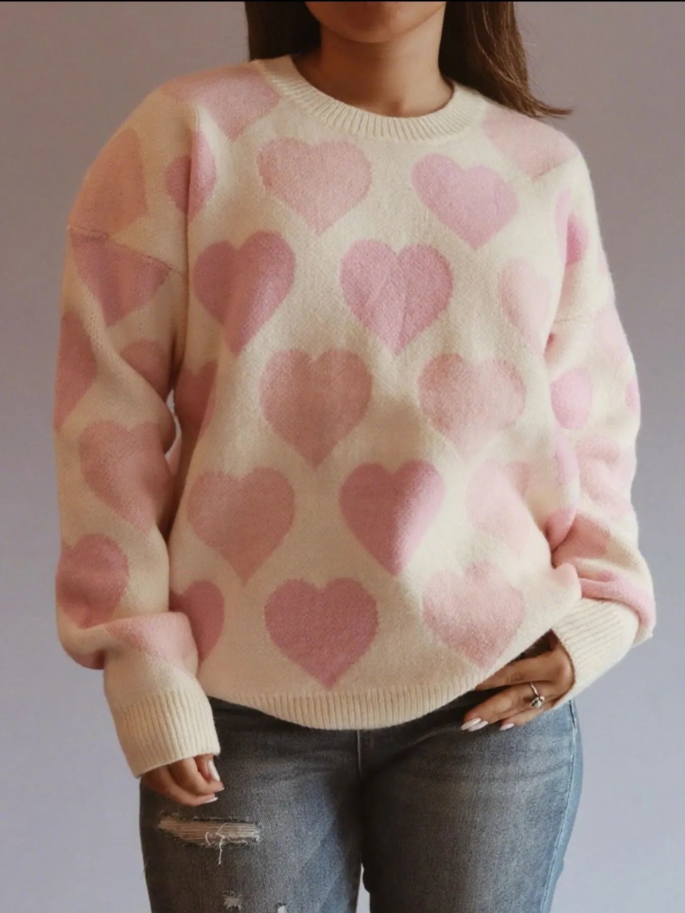 Person wearing a sweater with pink heart patterns on a plain background