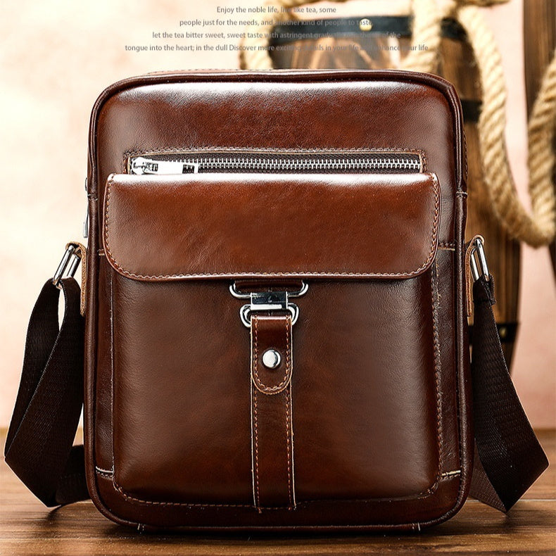Brown leather crossbody bag on a wooden surface with a blurred background