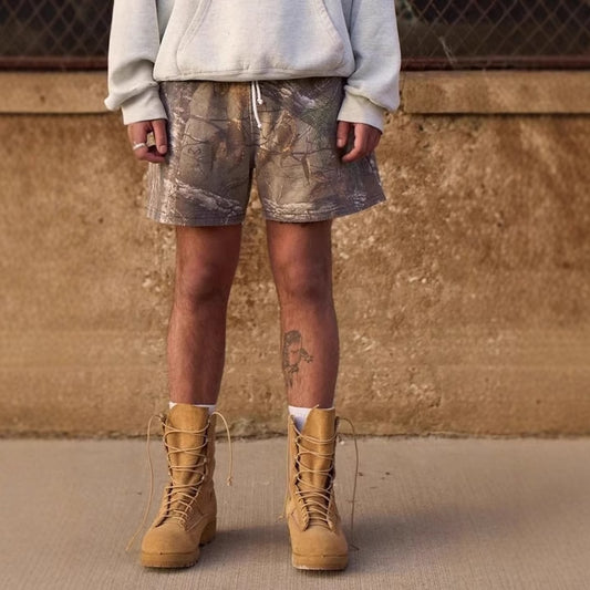 Person wearing camouflage shorts and tan boots against a brown wall.