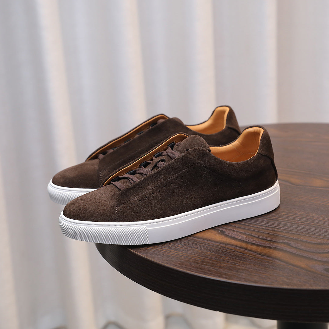 Brown suede sneakers with white soles on a wooden table against a neutral background