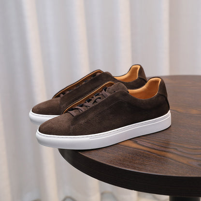 Brown suede sneakers with white soles on a wooden table against a neutral background