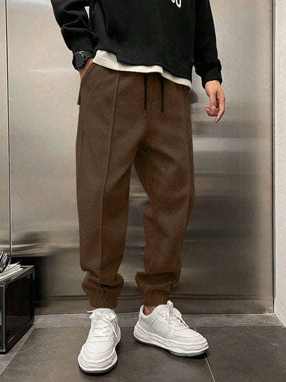 Person wearing brown pants and white sneakers in front of a metallic wall.