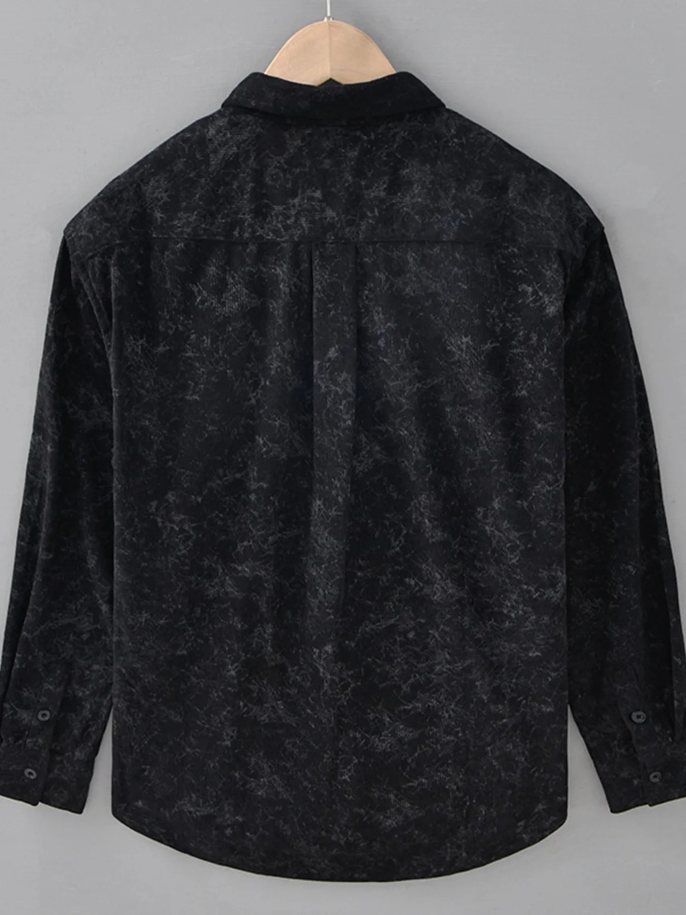 Black textured shirt on a hanger against a gray background