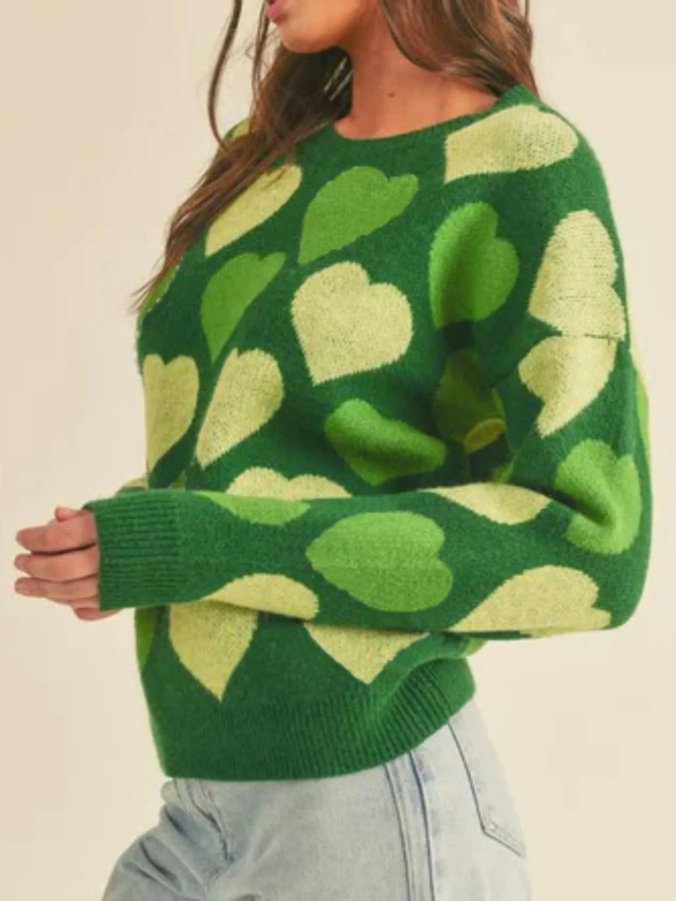 Green sweater with heart pattern worn by a person on a beige background