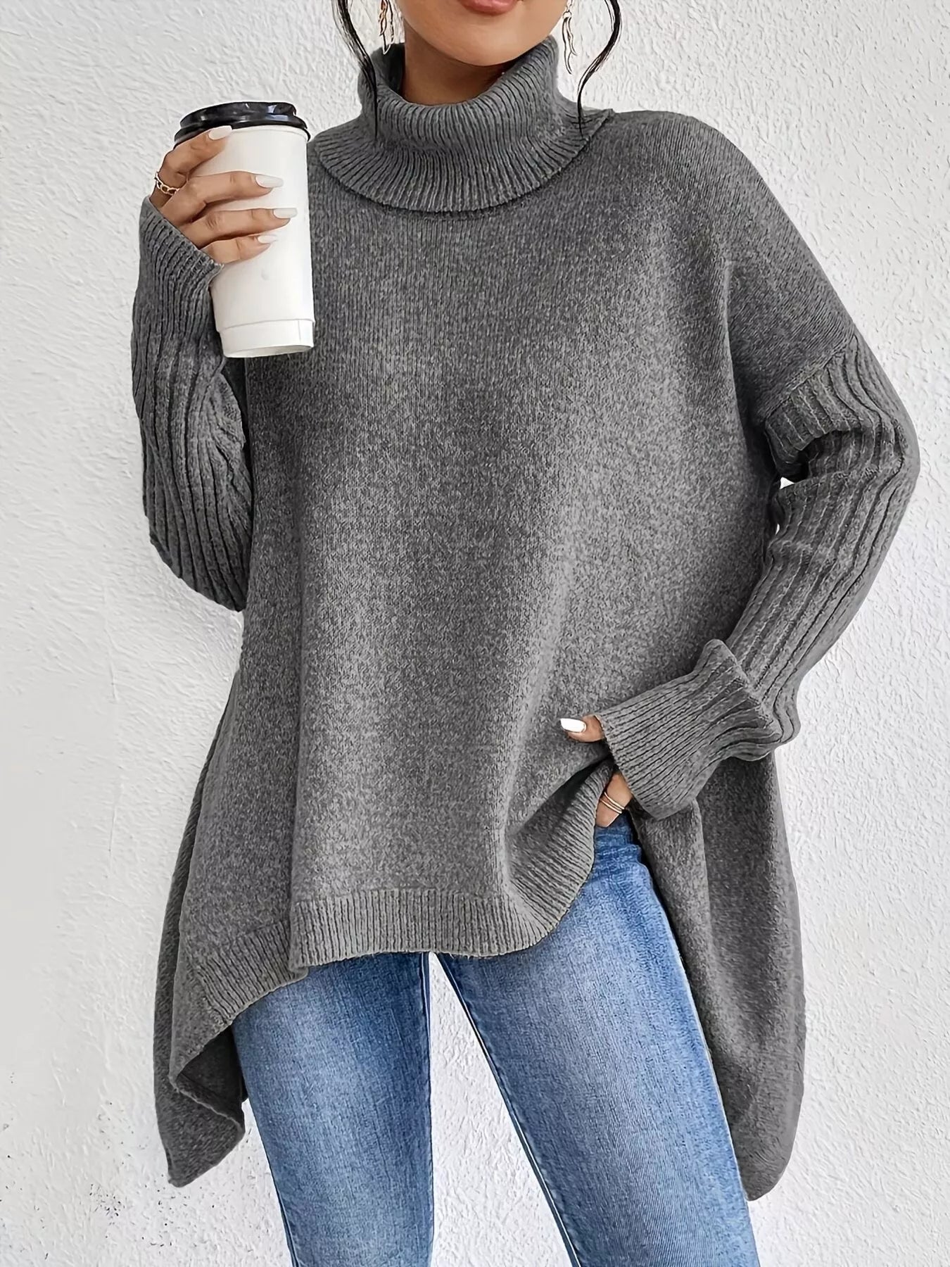 Person wearing a gray sweater holding a white cup against a light background