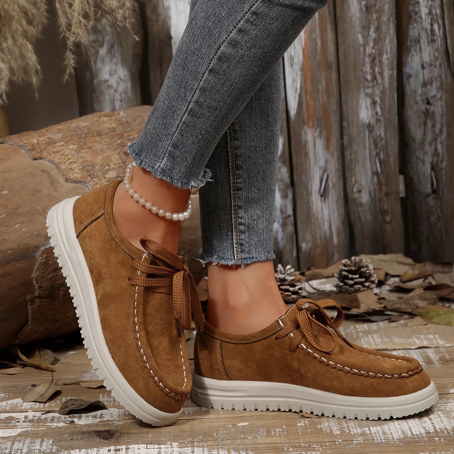 Brown suede shoes with white soles worn with blue jeans on a rustic wooden surface.