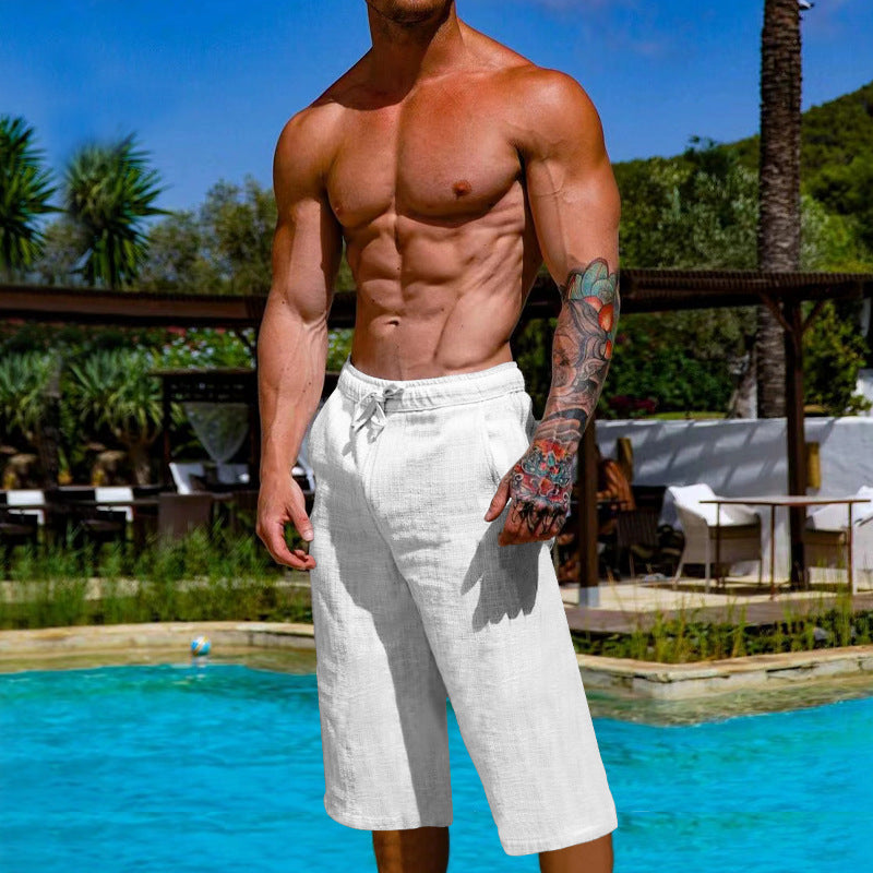 Muscular man in white shorts standing by a pool with a scenic background