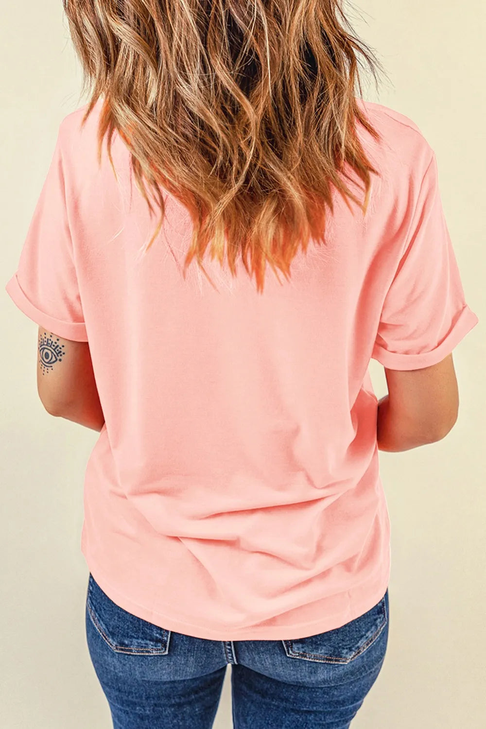 Person wearing a pink t-shirt and blue jeans against a beige background