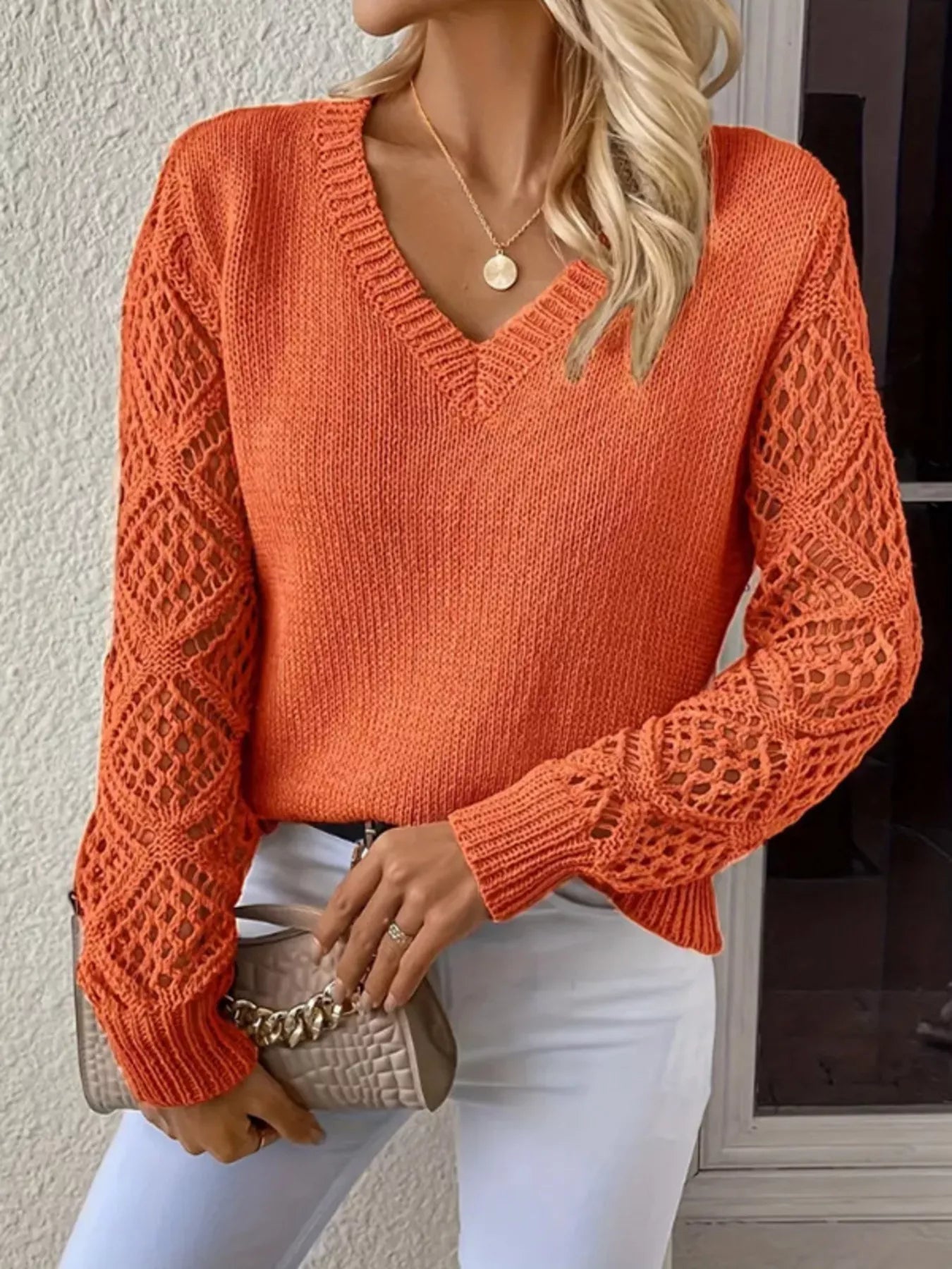 Person wearing an orange knitted sweater holding a beige handbag indoors.