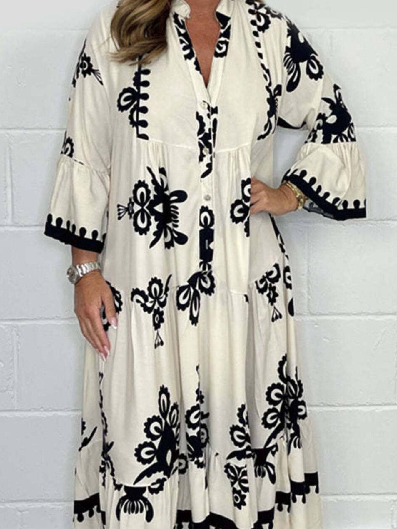 Woman wearing a long, patterned dress against a white wall.